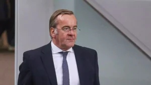 Boris Pistorius im dunklen Anzug und mit Krawatte vor neutralem Hintergrund.