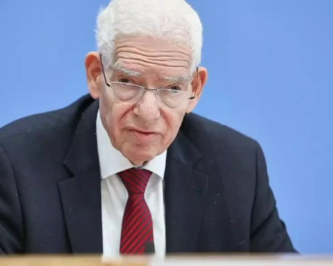 Josef Schuster sitzt im Anzug vor blauem Hintergrund und blickt ernst in die Kamera.