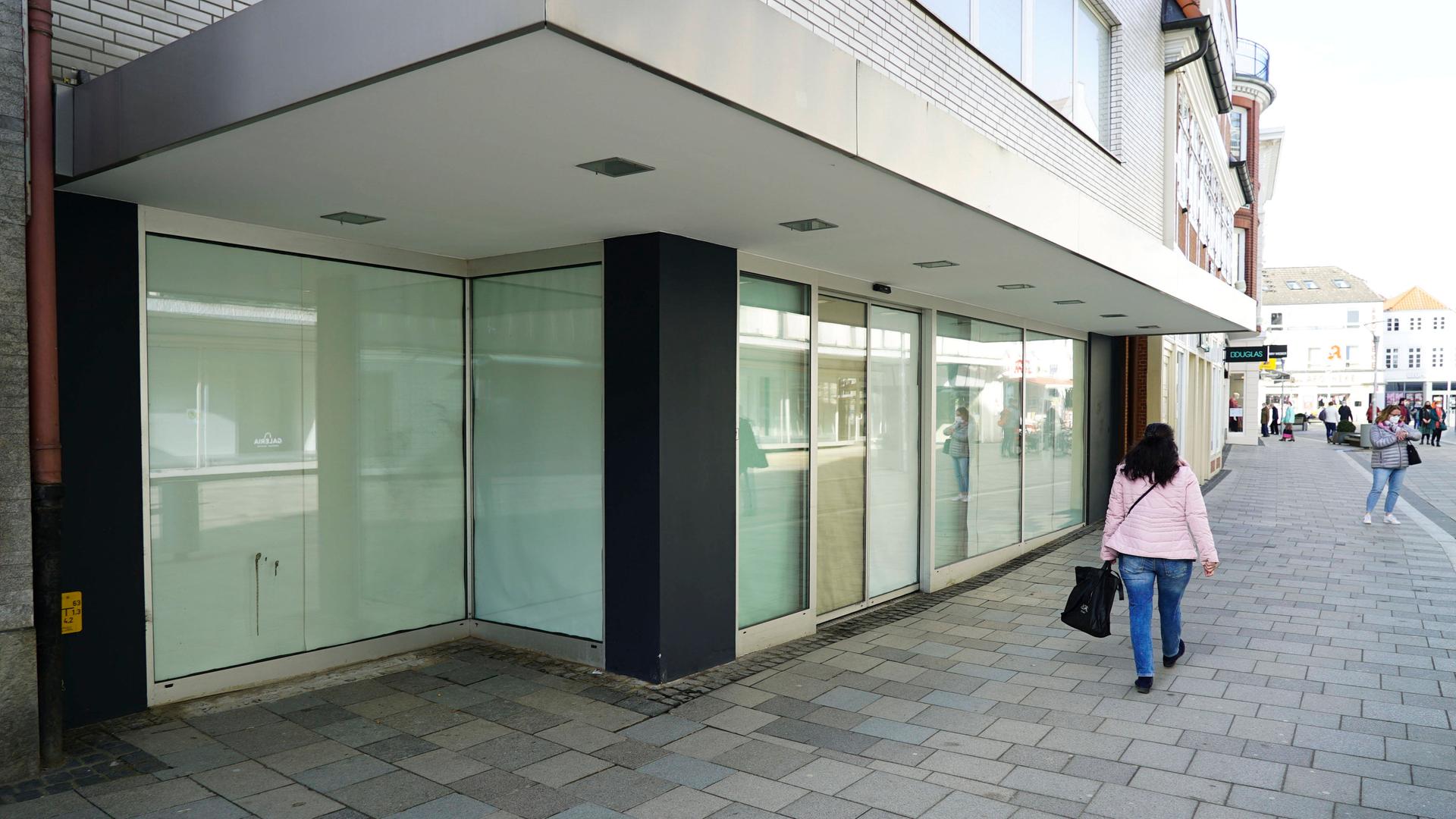 Galeria-Insolvenz erhöht Druck auf 83 Filialen in 70 Städten 1 Leerstehendes Ladenlokal mit großen Schaufenstern in einer Fußgängerzone, Passanten gehen vorbei.