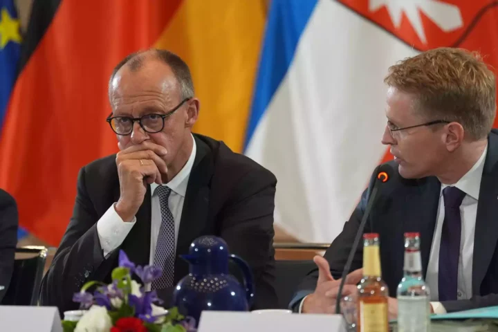 Daniel Günther sitzt bei einer Sitzung am Tisch und hört einem anderen Politiker zu.