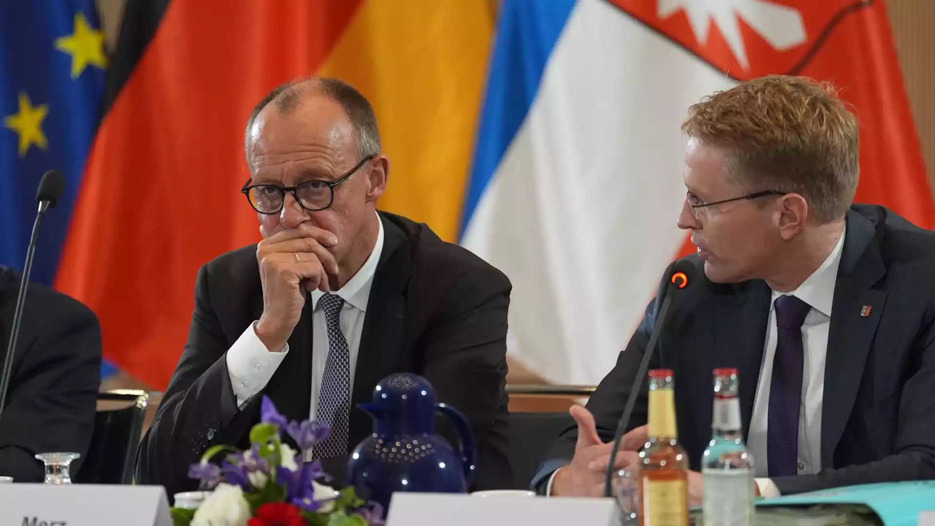 Daniel Günther sitzt bei einer Sitzung am Tisch und hört einem anderen Politiker zu.