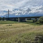 Autobahnbrücke über einer grünen Landschaft mit Wiesen und Wolkenhimmel.