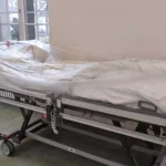 Ein mit Folie abgedecktes Krankenhausbett steht auf einem Stationsflur.