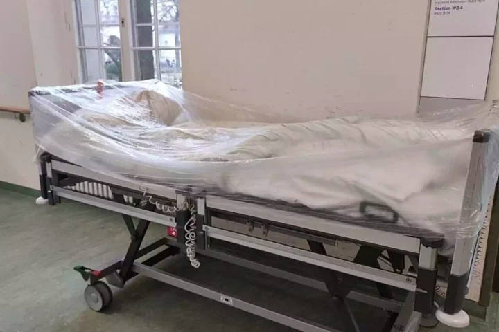 Ein mit Folie abgedecktes Krankenhausbett steht auf einem Stationsflur.
