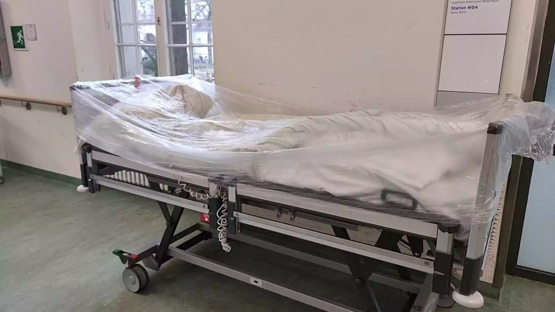 Ein mit Folie abgedecktes Krankenhausbett steht auf einem Stationsflur.