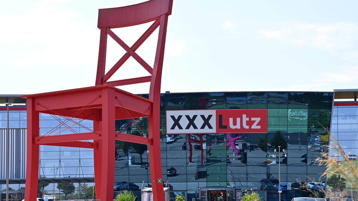 Großer roter Stuhl vor einem XXXLutz-Gebäude mit Firmenlogo.