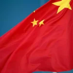 Chinesische Flagge weht vor blauem Hintergrund.