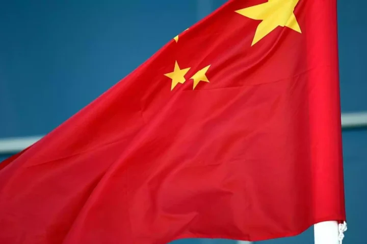 Chinesische Flagge weht vor blauem Hintergrund.