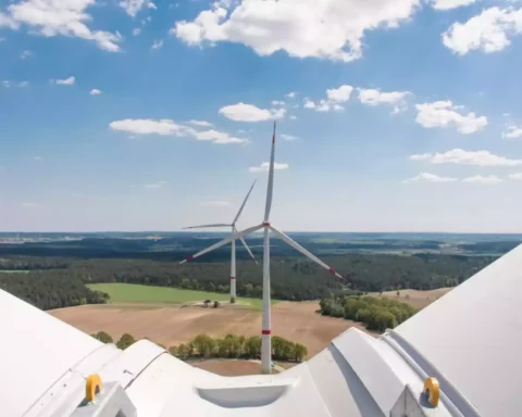 Blick von einer Windkraftanlage über Felder und Waldlandschaft unter blauem Himmel mit Wolken.
