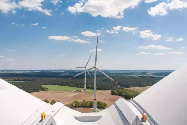 Blick von einer Windkraftanlage über Felder und Waldlandschaft unter blauem Himmel mit Wolken.