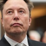 Elon Musk bei einem öffentlichen Auftritt in Anzug und Krawatte.