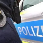 Nahaufnahme einer Polizeiuniform mit Handschellen vor einem Polizeiwagen.