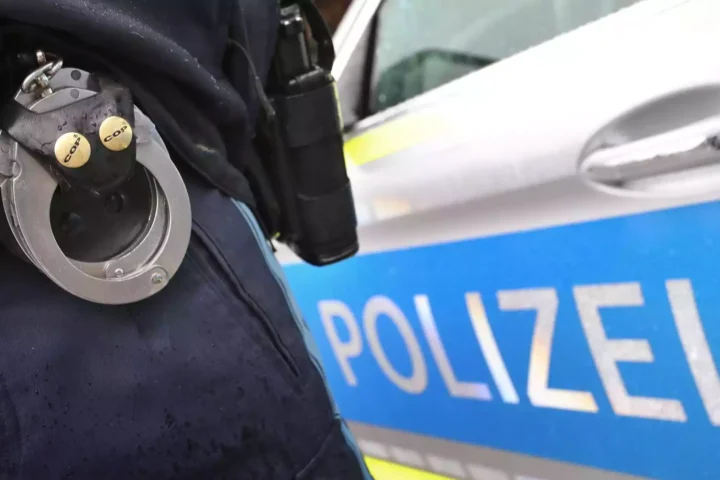 Nahaufnahme einer Polizeiuniform mit Handschellen vor einem Polizeiwagen.