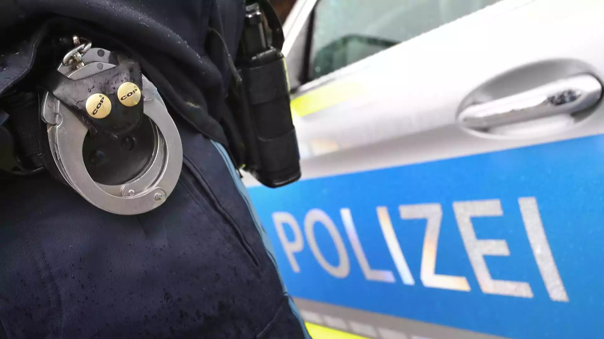 Bundesregierung meldet 148.311 offene Haftbefehle in Deutschland 1 Nahaufnahme einer Polizeiuniform mit Handschellen vor einem Polizeiwagen.
