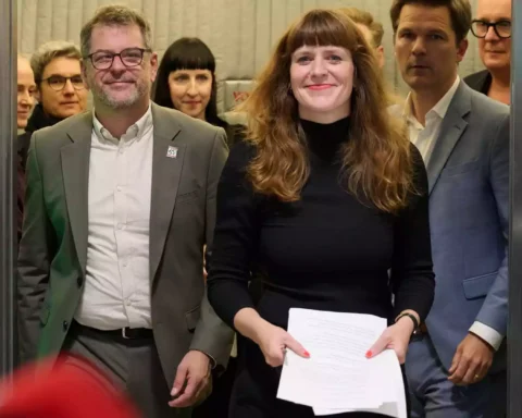Mehrere Politikerinnen und Politiker stehen in einem Innenraum zusammen, eine Frau hält Papiere in der Hand.
