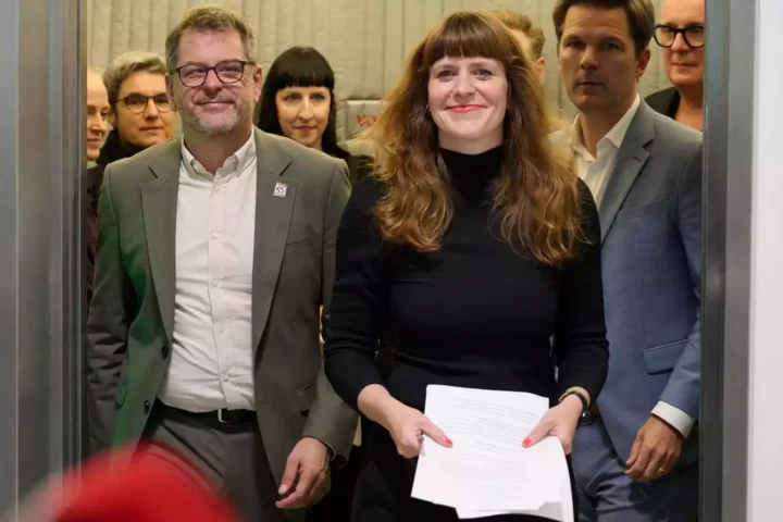 Mehrere Politikerinnen und Politiker stehen in einem Innenraum zusammen, eine Frau hält Papiere in der Hand.