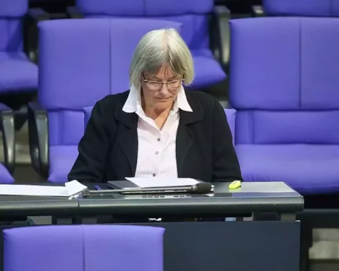 Eine Frau sitzt in einem parlamentarisch wirkenden Saal vor violetten Sitzen und blickt auf Unterlagen vor sich.