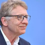 Porträt eines älteren Mannes mit Brille vor blauem Hintergrund.