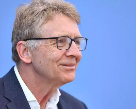 Porträt eines älteren Mannes mit Brille vor blauem Hintergrund.