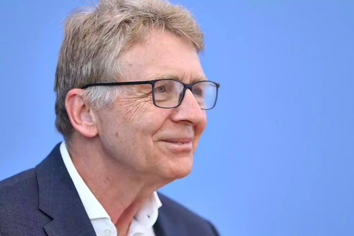Porträt eines älteren Mannes mit Brille vor blauem Hintergrund.