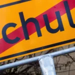 Nahaufnahme eines gelben Schulwegweisers mit dem Wort „Schule“.