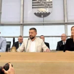 Mehrere Politiker sitzen an einem Sitzungstisch im Landtag, im Hintergrund das Wappen von Sachsen-Anhalt.