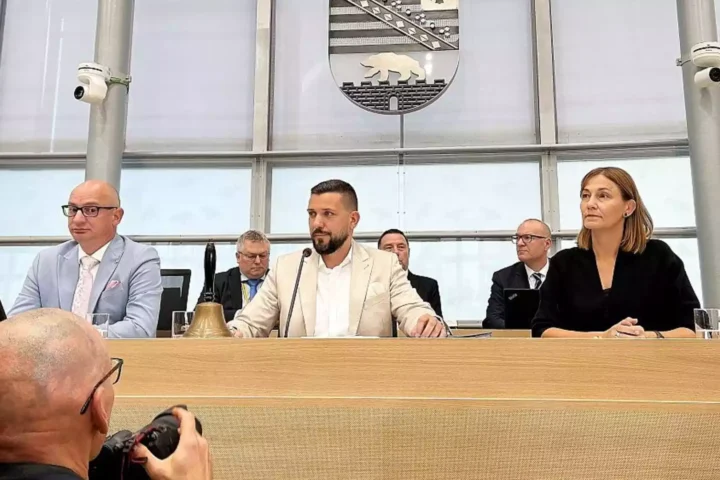 Mehrere Politiker sitzen an einem Sitzungstisch im Landtag, im Hintergrund das Wappen von Sachsen-Anhalt.