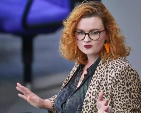 Eine Frau mit rotem, lockigem Haar und Brille spricht gestikulierend in einem Saal.