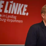 Ein Linke-Politiker steht vor einer roten Wand mit der Aufschrift „DIE LINKE. Fraktion im Landtag Mecklenburg-Vorpommern“.