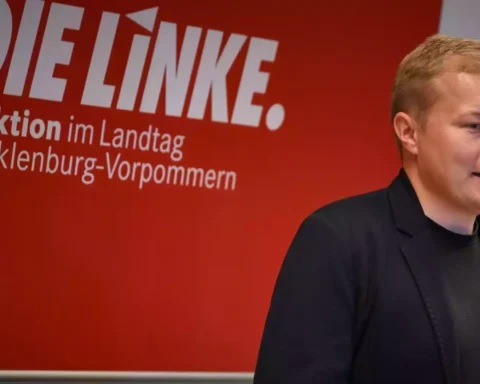 Ein Linke-Politiker steht vor einer roten Wand mit der Aufschrift „DIE LINKE. Fraktion im Landtag Mecklenburg-Vorpommern“.