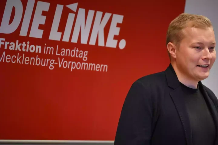Ein Linke-Politiker steht vor einer roten Wand mit der Aufschrift „DIE LINKE. Fraktion im Landtag Mecklenburg-Vorpommern“.