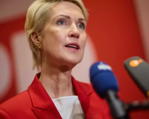 Eine blonde Frau spricht bei einer Pressekonferenz vor mehreren Mikrofonen.
