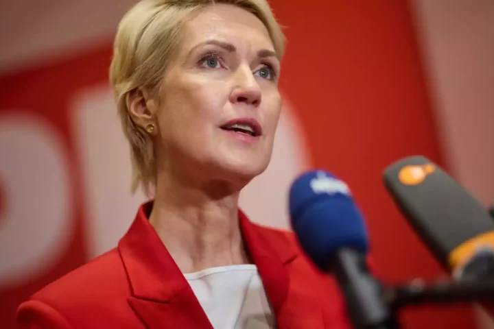 Eine blonde Frau spricht bei einer Pressekonferenz vor mehreren Mikrofonen.