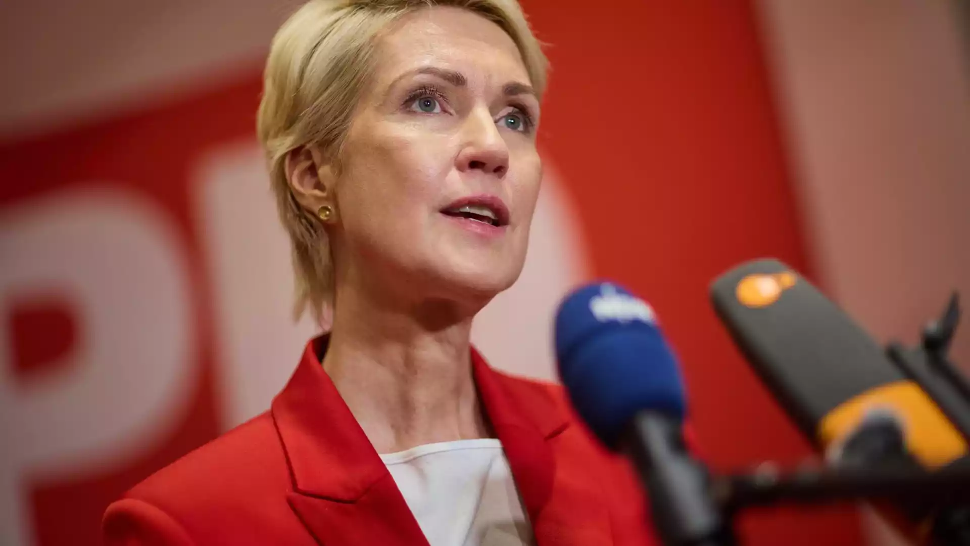 Eine blonde Frau spricht bei einer Pressekonferenz vor mehreren Mikrofonen.