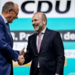 Zwei CDU-Politiker schütteln sich auf einer Bühne vor einem CDU-Hintergrund die Hand.