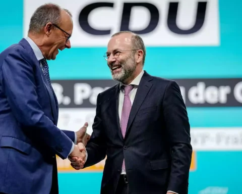 Zwei CDU-Politiker schütteln sich auf einer Bühne vor einem CDU-Hintergrund die Hand.