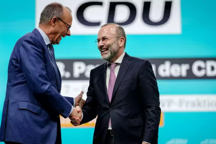 Zwei CDU-Politiker schütteln sich auf einer Bühne vor einem CDU-Hintergrund die Hand.