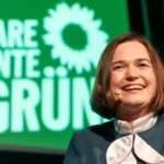 Eine Frau spricht mit Headset-Mikrofon vor einem grünen Hintergrund mit Grünen-Logo und dem Schriftzug „KlaRe Kante GRÜN“.