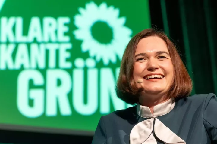 Eine Frau spricht mit Headset-Mikrofon vor einem grünen Hintergrund mit Grünen-Logo und dem Schriftzug „KlaRe Kante GRÜN“.