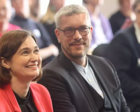Zwei Politiker sitzen bei einer Veranstaltung und lächeln in den Raum.