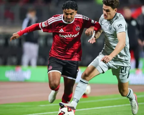 Zwei Fußballspieler von 1. FC Nürnberg und VfL Wolfsburg kämpfen am Ball auf dem Spielfeld.