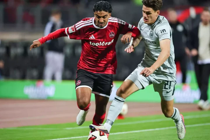 Zwei Fußballspieler von 1. FC Nürnberg und VfL Wolfsburg kämpfen am Ball auf dem Spielfeld.