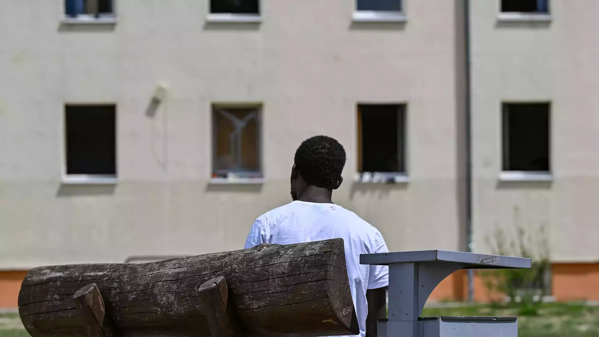 Bundesweite Asylklagen dauern länger, Sachsen liegt bei 20,4 Monaten hinten 1 Ein Mann sitzt auf einer Bank vor einem Gebäude und blickt auf die Fassade.