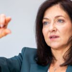 Katherina Reiche spricht vor hellem Hintergrund und hebt eine Hand.