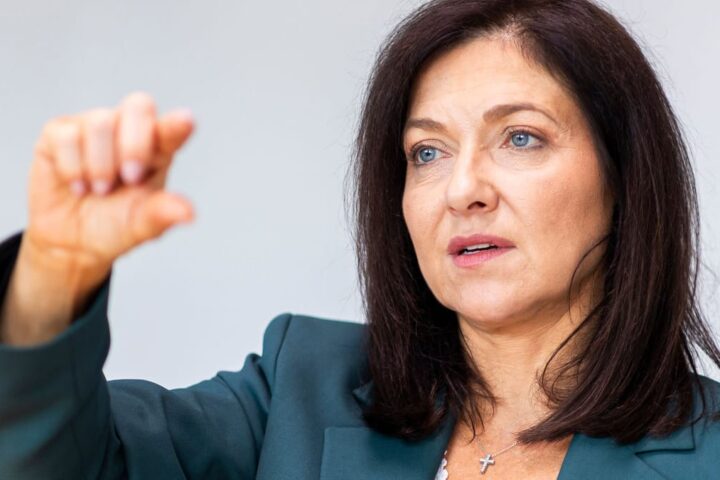 Katherina Reiche spricht vor hellem Hintergrund und hebt eine Hand.