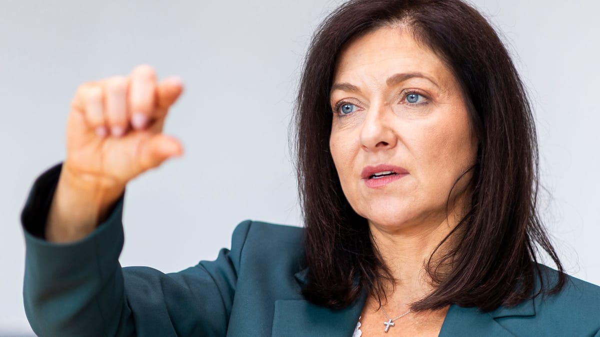 Katherina Reiche spricht vor hellem Hintergrund und hebt eine Hand.