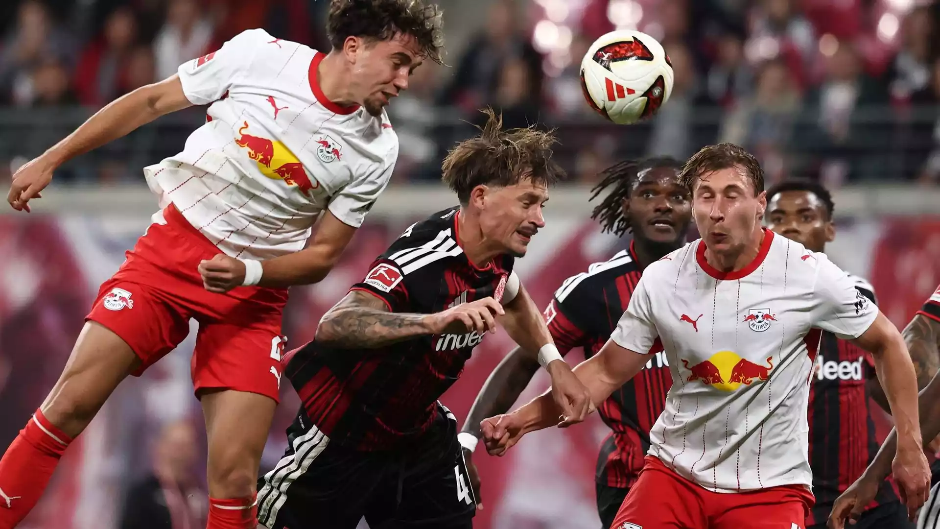Spieler von RB Leipzig und Eintracht Frankfurt kämpfen im Kopfballduell um den Ball.
