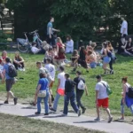 Junge Menschen sitzen und gehen auf einer Wiese in einem Park.