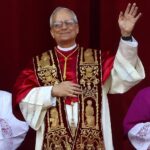 Papst Leo XIV. winkt in liturgischer Kleidung vor rotem Hintergrund.