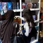 Zwei Frauen betrachten an einem Bücherstand farbig gestaltete Romane.